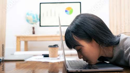 Stressed tired Asian businesswoman feels exhausted sitting at office desk with laptop and crumpled paper, frustrated woman can not concentrate having writers block, lack of new ideas creative crisis