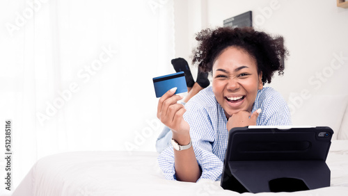 Beautiful African woman holding a credit card by fingers in hands.Happy online shopping payment internet banking using online banking.Joyful beautiful cheering female in bedroom house.