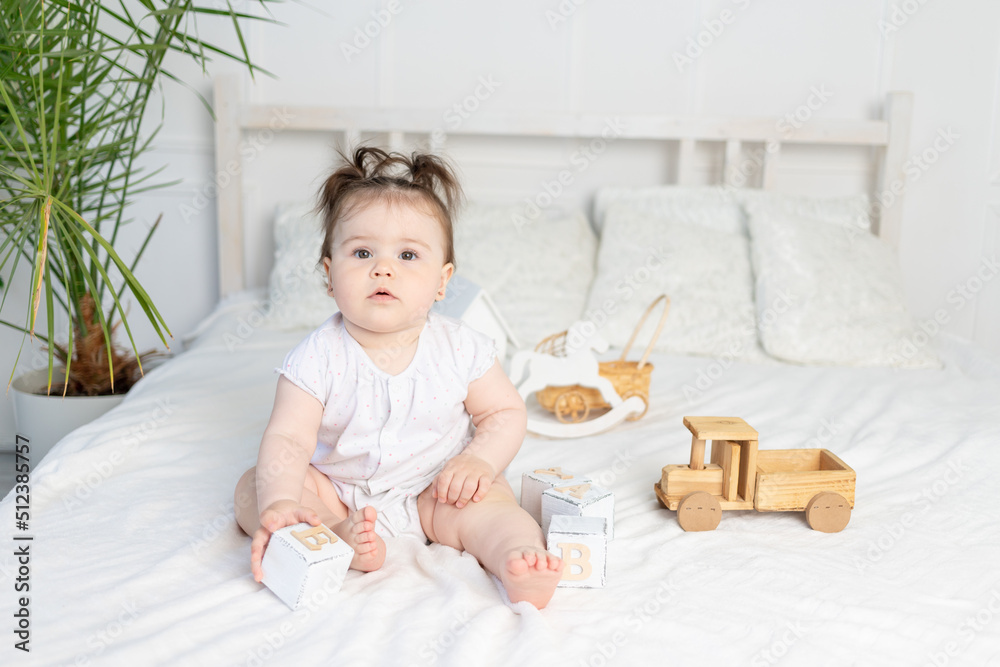 baby girl playing with wooden toy cubes on the bed at home in a bright room, the concept of early childhood development baby girl playing with wooden toy cubes on the bed at home in a bright room, the concept of early childhood development
