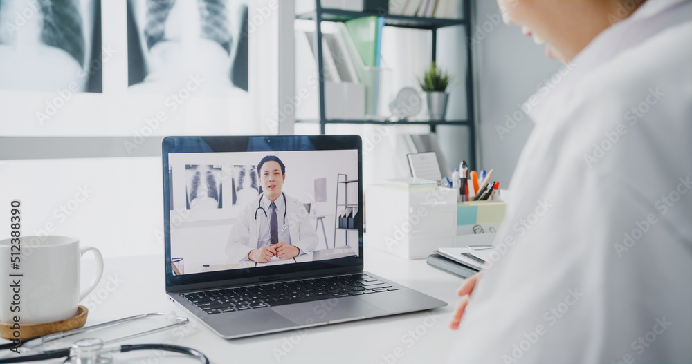 Young Asia lady doctor in white medical uniform using laptop talking video conference call with senior doctor at desk in health clinic or hospital. Social distancing, quarantine for corona virus. Young Asia lady doctor in white medical uniform using laptop talking video conference call with senior doctor at desk in health clinic or hospital. Social distancing, quarantine for corona virus.