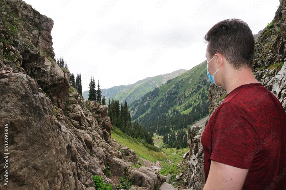 Naklejka premium The guy in the mountains takes off his medical mask. Recovery from the coronavirus, the epidemic, and just the virus. A fresh breath of air. Sense of freedom. Forest, mountains, grass and sky.