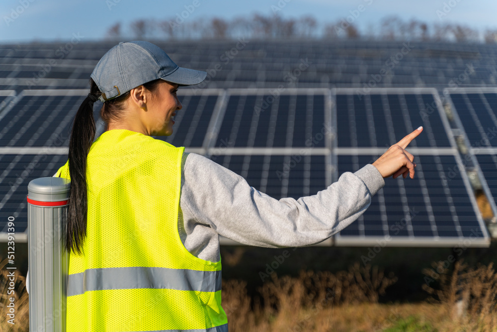 Back view of the female ecological engineer pointing away while collects efficient information about solar panels. Photovoltaic solar farm, green energy, environment concept Back view of the female ecological engineer pointing away while collects efficient information about solar panels. Photovoltaic solar farm, green energy, environment concept