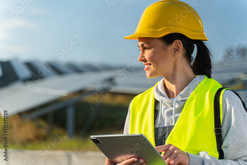 Caucasian female engineer in special uniform using tablet while standing with solar panel at the background. Concept of alternative electricity