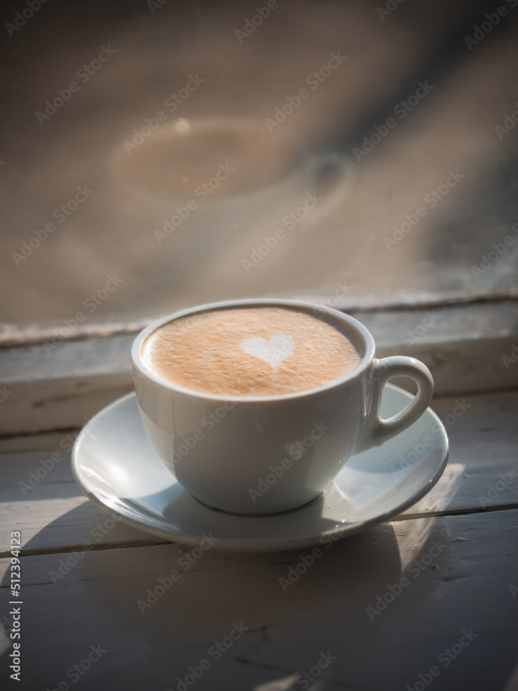 Obraz premium Cup of cappuccino with latte art in the shape of a heart by the window