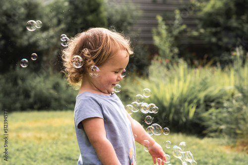 Toddler girl playing with bubbles in backyard on summer day