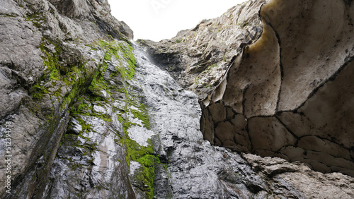 Ice grotto, a snow cave in the mountains in summer. Drops drip from the edges of the walls. Huge snow tunnel. Large rocks and rocks. Moss and grass grow in places. Thick walls of snow. Unusual place.