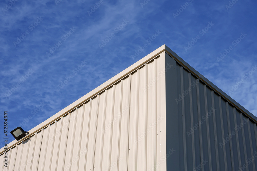 Sunlight on surface of white corrugated steel warehouse wall against clouds on blue sky in low angle view Sunlight on surface of white corrugated steel warehouse wall against clouds on blue sky in low angle view