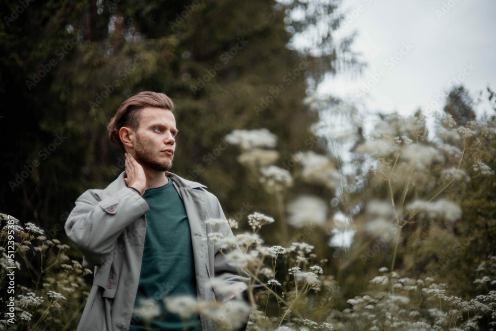man in a gray coat in the summer in the forest grass and trees. The concept of the philosopher's walk in nature, nostalgia and memories.