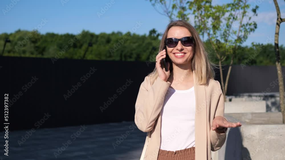 Adult Energetic Confident Young Woman Talking on Mobile Phone Outside near Park. Charismatic girl is having friendly call with friend or family, actively gestures with hands during the conversation. Adult Energetic Confident Young Woman Talking on Mobile Phone Outside near Park. Charismatic girl is having friendly call with friend or family, actively gestures with hands during the conversation.