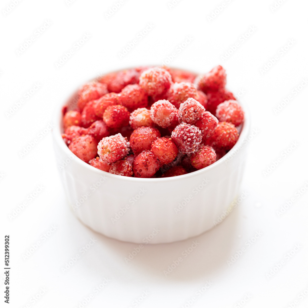 Frozen red wild forest strawberry in white bowl on white. Selective focus. Square photo. Frozen red wild forest strawberry in white bowl on white. Selective focus. Square photo.