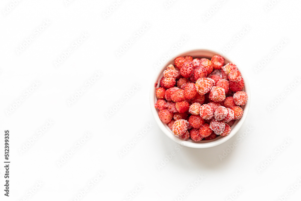 Frozen red wild forest strawberry in white bowl on white background. Copy space. Top view. Frozen red wild forest strawberry in white bowl on white background. Copy space. Top view.