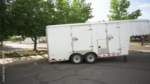 Small white gooseneck cargo trailer in an empty parking lot, pan