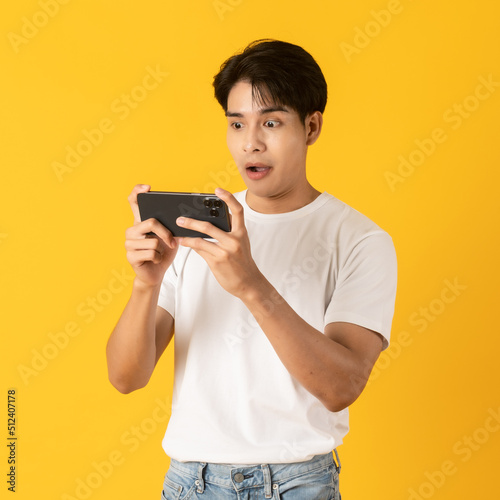 Young good looking asian man using smartphone isolated on yellow background with surprise
