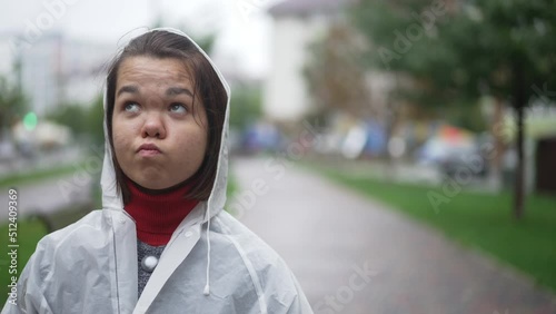 Portrrait of upset little woman looking up standing on the right in overcast city. Sad Caucasian little person in rain coat thinking spending weekend on rainy day outdoors photo