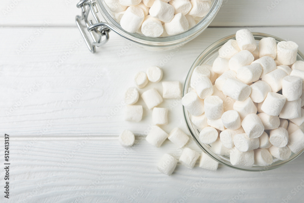 Marshmallows in a glass bowl and jar on a white textured table.Sweets and snacks for a snack.Chewy candy close-up.Copy space.Place for text.