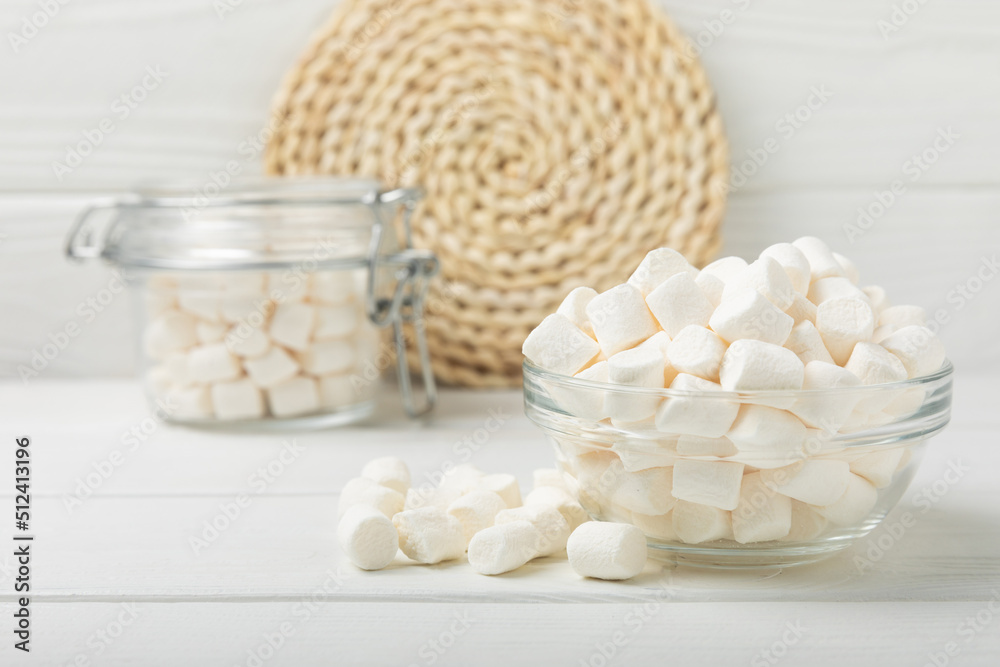 Marshmallows in a glass bowl and jar on a white textured table.Sweets and snacks for a snack.Chewy candy close-up.Copy space.Place for text.