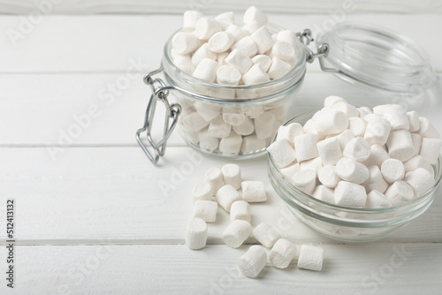 Marshmallows in a glass bowl and jar on a white textured table.Sweets and snacks for a snack.Chewy candy close-up.Copy space.Place for text.