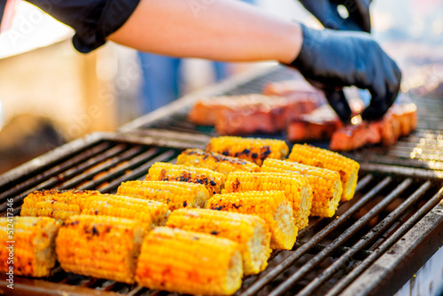 BBQ corn. Hands in gloves flip corn on an open barbecue fire. Corn on a charcoal grill.Picnic in the backyard during a family holiday.
