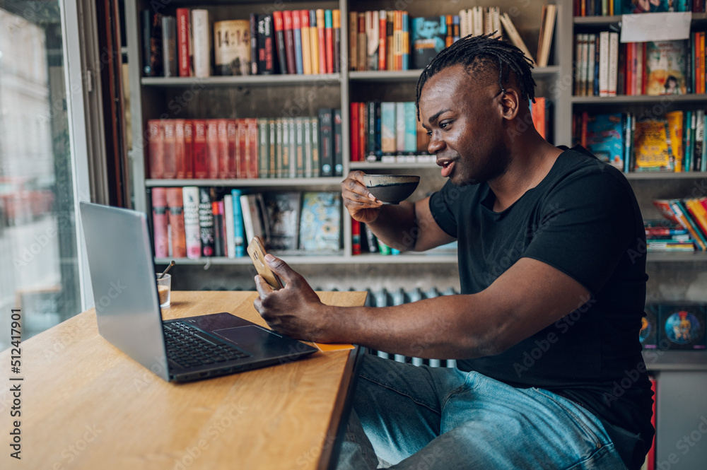 African american man using laptop while drinking coffee in a cafe African american man using laptop while drinking coffee in a cafe