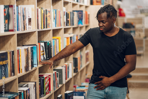 African american man picking and reading books in library or bookstore