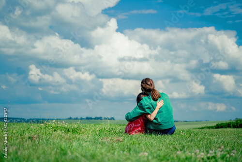 Back view of two young girls sisters hug each other in the green field. Love, happy childhood concept.