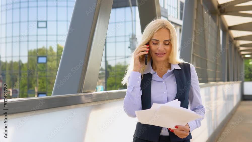 Portrait of business woman with documents calling phone outdoor. Businesswoman talking mobile phone near modern office building