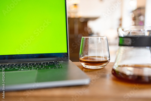 Cozy cafe atmosphere with a glass of coffee, carafe and a laptop with a green screen on the wooden table