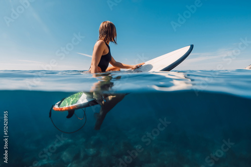 Sporty surf girl in bikini sitting on surfboard, split view in ocean