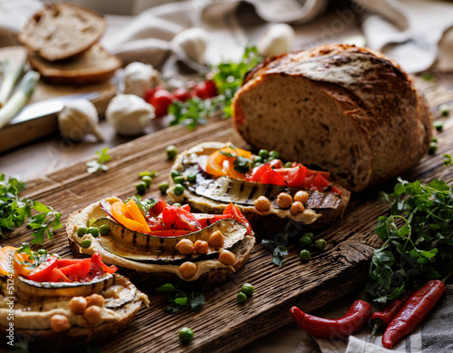 Sourdough bread open faced sandwiches with hummus, grilled zucchini and tomatoes on a rustic board, close up view. A healthy and delicious vegetarian food