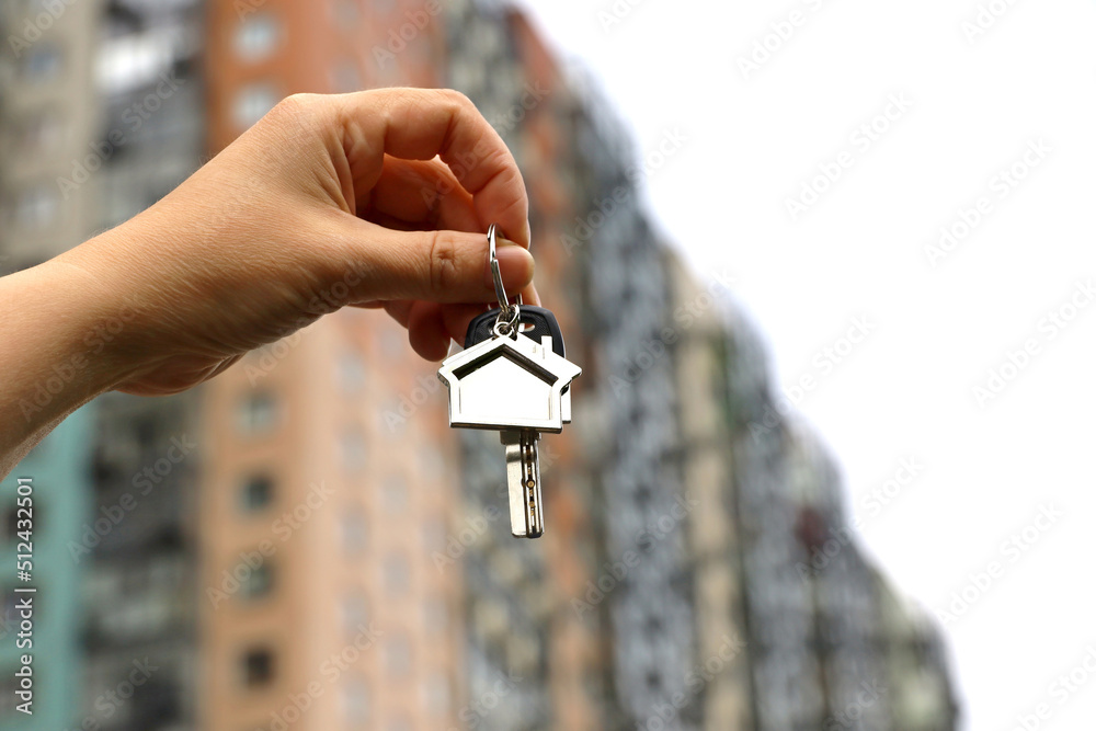 Real estate agent, home keys in female hand on background of new building. Byung apartment or renting property Real estate agent, home keys in female hand on background of new building. Byung apartment or renting property