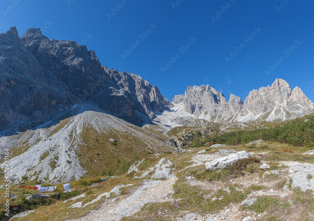 Rocky dolomite ridges overlooking the Vallon Popera in Comelico region with green meadows, blue sky and the hanging clothes of the Berti Hut, Dolomites, Italy