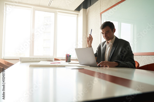 Designer holding pencil while working on laptop at table