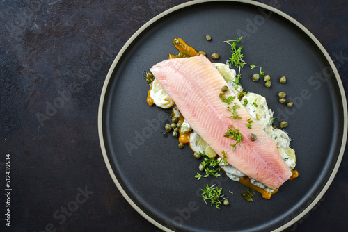 Modern style traditional smoked rainbow trout with boiled potato salad, yoghurt and mustard served as top view on a Nordic design plate with copy space photo