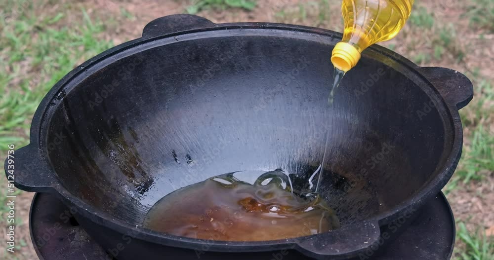 Cook pours oil into the cauldron a before cooking pilaf Cook pours oil into the cauldron a before cooking pilaf