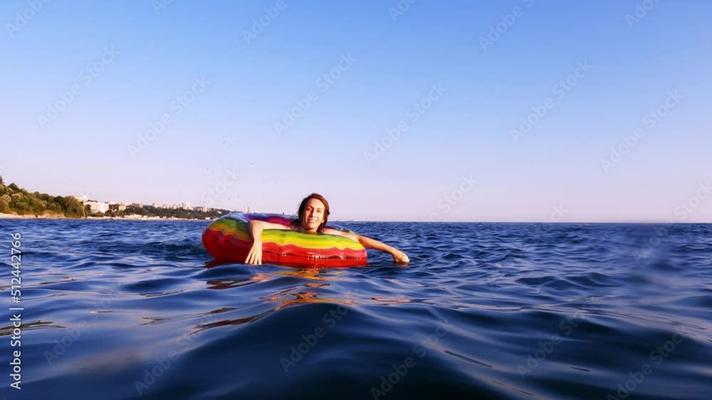 A woman swims in an inflatable bright life buoy in the blue sea enjoying the summer sun. Sea relaxation. A woman swims in an inflatable bright life buoy in the blue sea enjoying the summer sun. Sea relaxation.