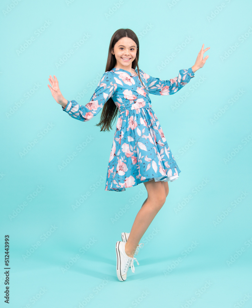 Full length cheerful teenager kid jump enjoy rejoice win isolated on blue background. Small child girl in summer dress jumping. Full length cheerful teenager kid jump enjoy rejoice win isolated on blue background. Small child girl in summer dress jumping.