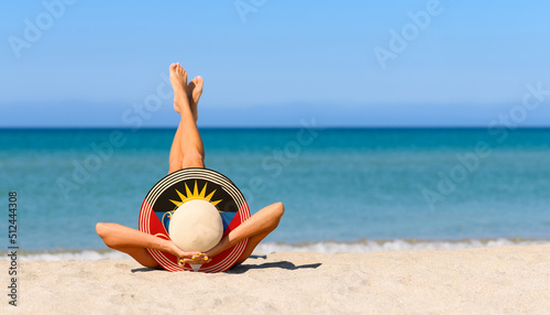 Fototapeta Naklejka Na Ścianę i Meble -  A slender girl on the beach in a straw hat in the colors of the Antigua and Barbuda flag. The concept of a perfect vacation in a resort in the Antigua and Barbuda. Focus on the hat.