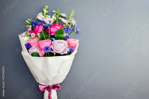 Fresh bouquet of roses foxgloves bachelor buttons flowers wrapped in paper and arranged on background. photo