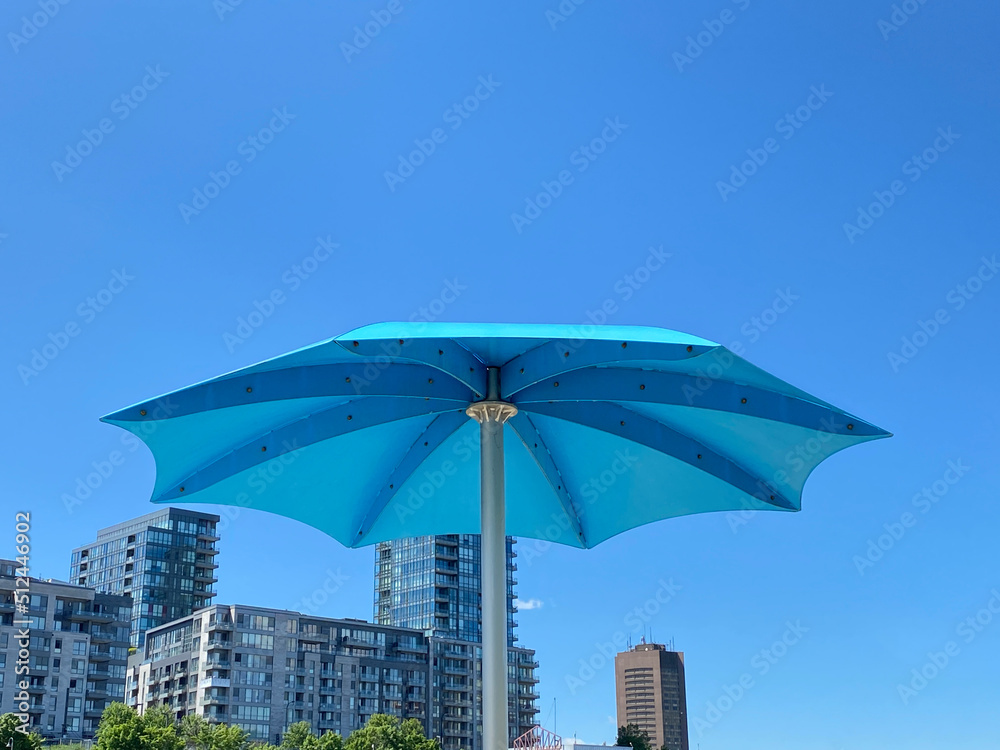 Parasol de plage en métal turquoise sur un fond de ciel bleu dans la ville  en été. Vue en contre-plongée d'un ombrelle contre les gratte-ciel dans une  zone urbaine. Stock Photo