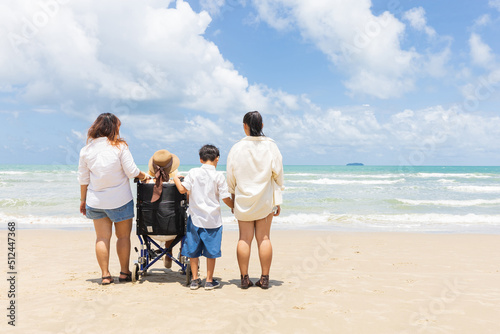 back view woman in a wheelchair with family and looking to sea on the beach
