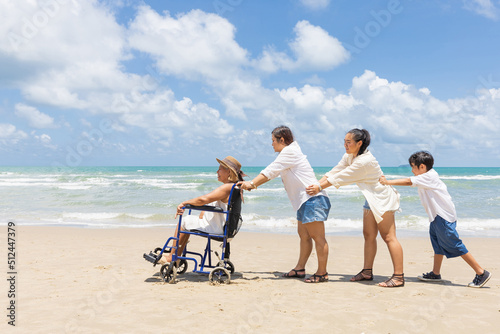 senior woman in a wheelchair with family helping and support on the beach