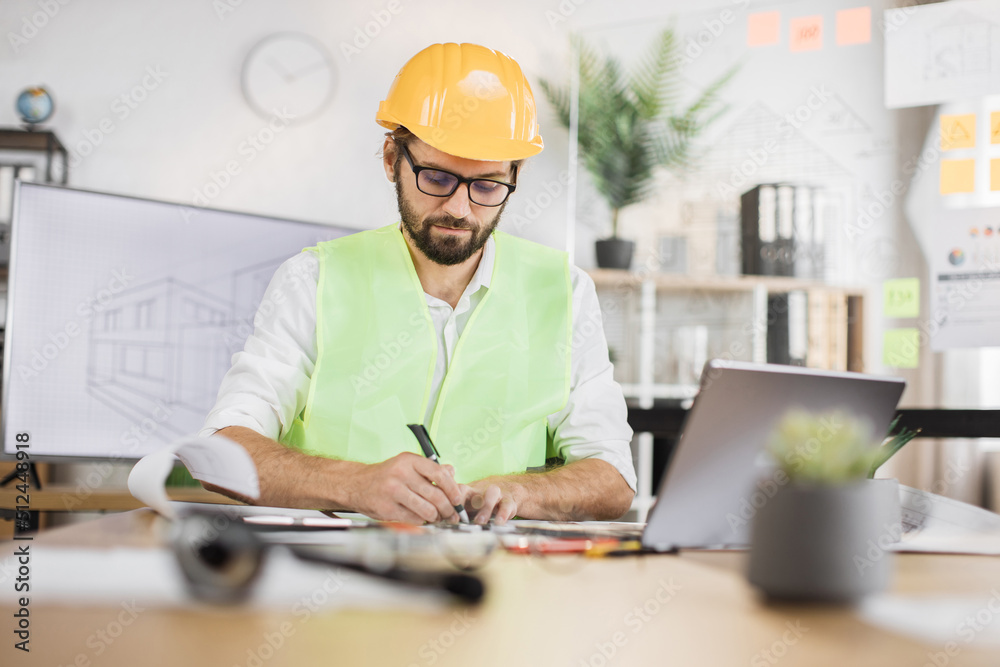 Architect man or male builder hold pen and ruler, writing and drawing architectural project, work on laptop computer on the desk at workplace. Architect man or male builder hold pen and ruler, writing and drawing architectural project, work on laptop computer on the desk at workplace.
