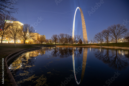 Reflection of glowing Gateway Arch of St. Louis with spot lights on surface of lake at sunset time on National Park
