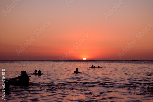 Fototapeta Naklejka Na Ścianę i Meble -  Relajante atardecer con siluetas de personas nadando en la playa de Santa Marta en Colombia