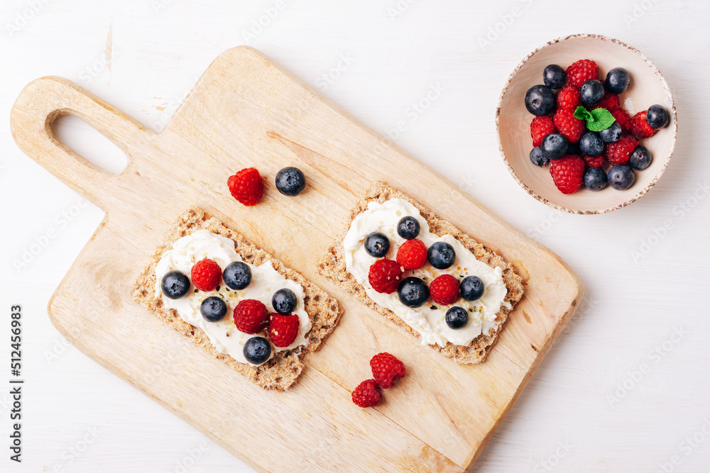 Sandwiches with blueberries and raspberries on cutting board on white wooden table. Healthy breakfast. Top view, flat lay Sandwiches with blueberries and raspberries on cutting board on white wooden table. Healthy breakfast. Top view, flat lay