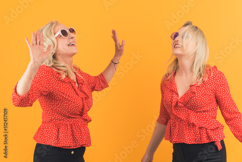 Studio shot of two funny happy blonde women in their 40s wearing red shirts with white dots and black trousers having fun and dancing toghether. High quality photo