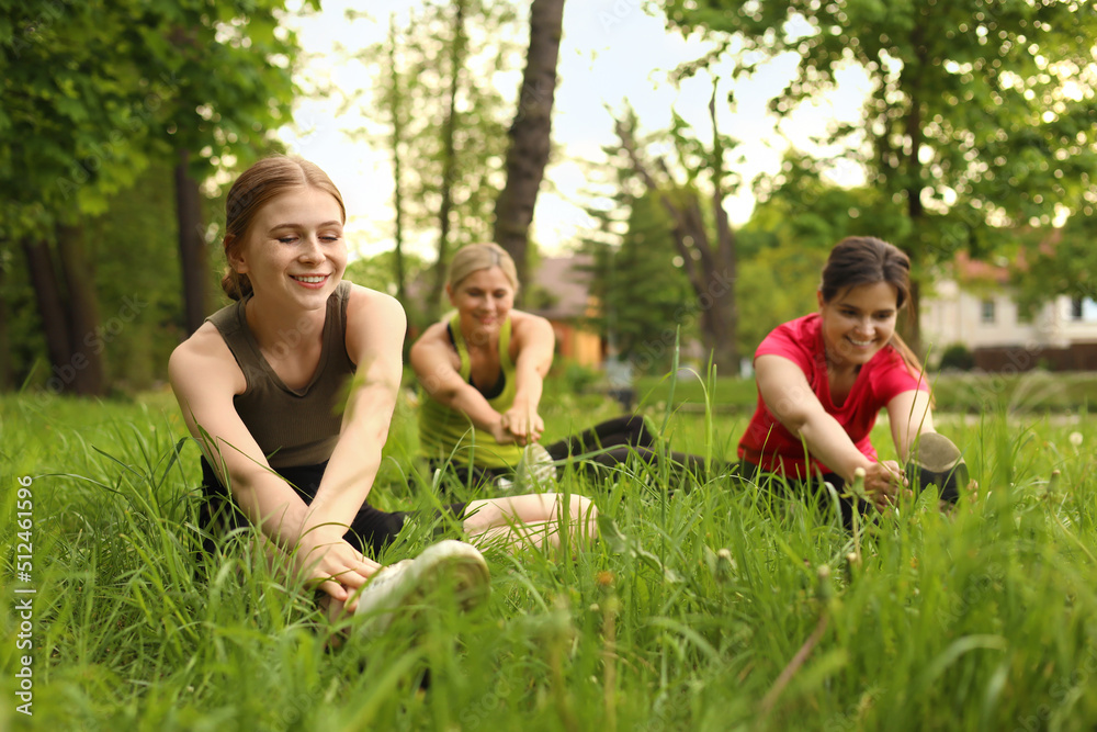 Fototapeta premium Women and teenage girl doing morning exercise on green grass in park