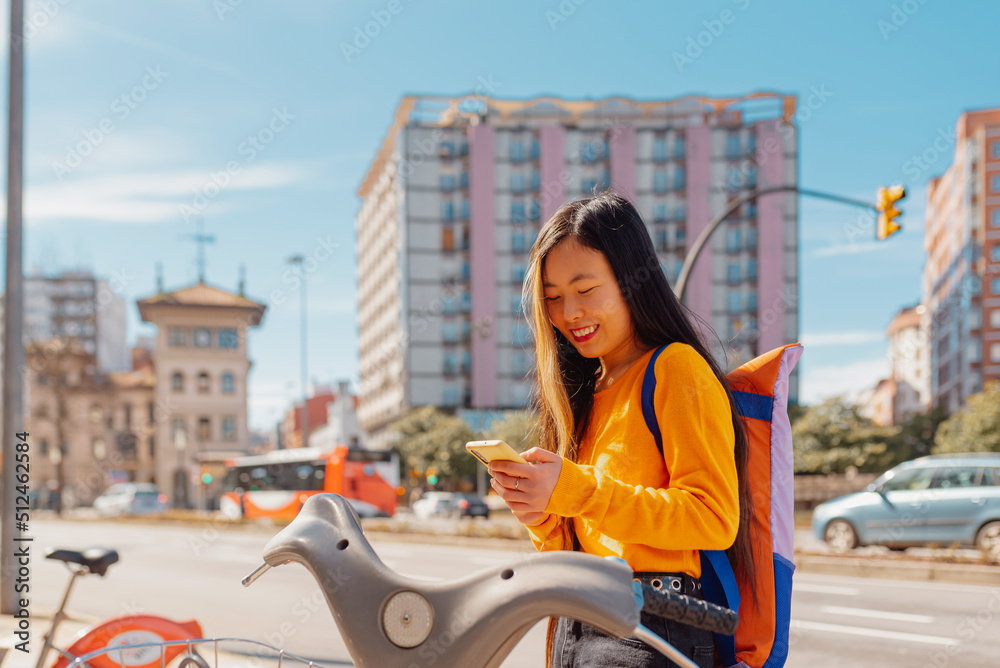 Asian girl using an app on her mobile phone to rent a bike to ride around the city. sustainable cities and ecological transport.