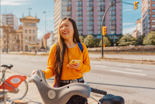 young asian woman using an app on her smartphone to pay for a bike rental for urban mobility. sustainable cities and ecological transport.