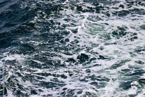 Stern waves with white foam tips on greyish blue sea water, photo taken from aboard ship. Selective focus